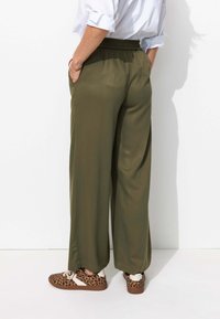 Pantalons large en vert olive avec une taille élastique et des poches latérales, associés à des baskets à imprimé animal. Tissu lisse et léger.