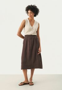 Top sans manches en tricot blanc avec un décolleté en V profond et trois boutons, associé à une jupe midi marron fluide dotée d'une taille élastique.