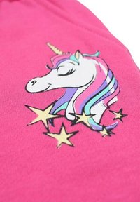 Le tissu rose présente un motif de licorne avec une crinière multicolore et des étoiles, le tout imprimé en noir et jaune, créant un contraste avec le fond.