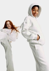 Felpa con cappuccio grigio in pile e pantaloni abbinati su due bambini. Un bambino indossa una maglietta bianca. Vestibilità casual con tasche e texture morbida.