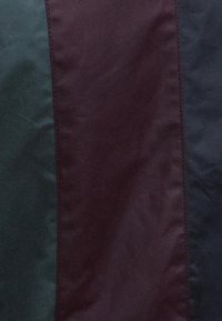 Sötétzöld, bordó és tengerészkék többszörös panelekből álló szövet. Simára varrt szélű, enyhén fényes textúrájú.