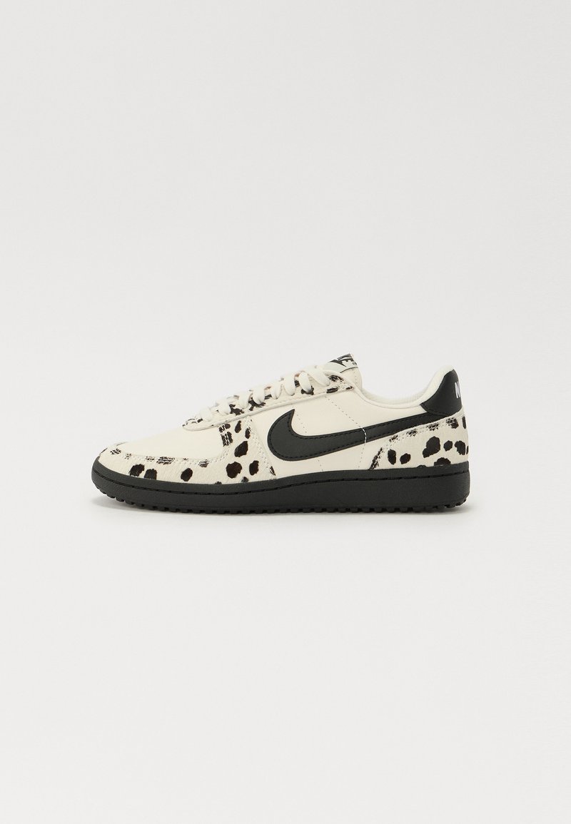 Tenisii albi cu un model cu pete negre, Swoosh-ul Nike negru, șireturi plate și o talpă din cauciuc negru. Design clasic de tip low-top.