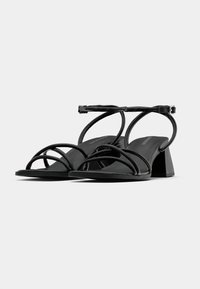 Black heeled sandals featuring a wide strap design with multiple thin crossing bands. Made of smooth material with a matte finish.