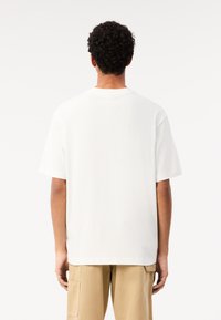 Camiseta blanca de manga corta con cuello redondo y un corte holgado. Tejido suave, costuras mínimas y diseño liso, combinada con pantalones beige.