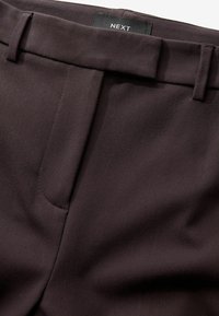 Pantalons ajustés marron foncé en tissu lisse et texturé, avec un devant plat, des passants de ceinture et une étiquette NEXT sur la taille.