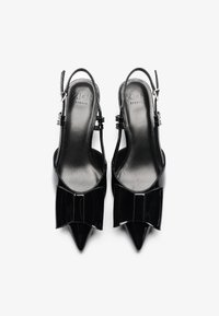 Scarpe slingback in vernice nera con punte affusolate, caratterizzate da un dettaglio a fiocco sulla parte anteriore e cinturini regolabili con fibbia.