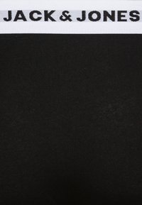 Tissu en coton noir avec une taille élastique blanche portant l'inscription "JACK & JONES" imprimée en noir. Texture lisse, design ajusté.