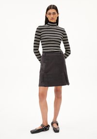 Zwart-wit gestreepte coltrui, aansluitend design. Donkere corduroy A-lijn rok met zakken. Platte zwarte schoenen met decoratieve bandaccenten.