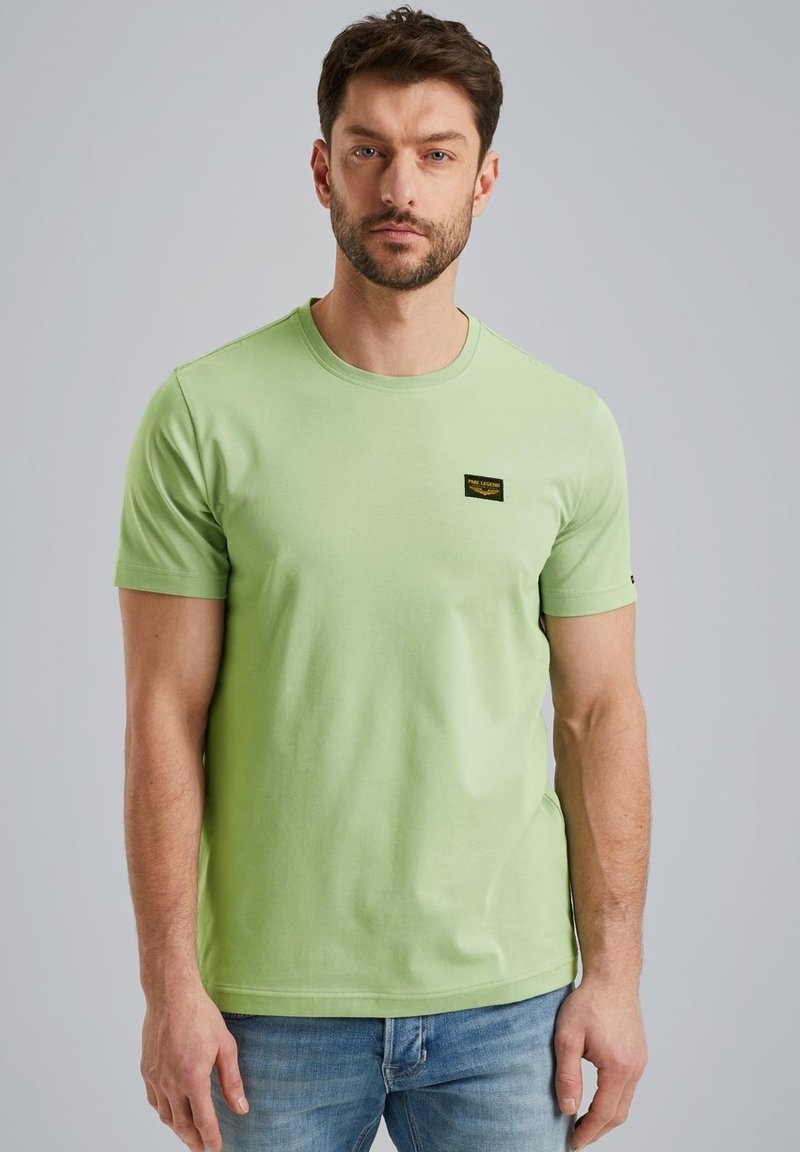 Camiseta de algodón de manga corta en verde claro, con una pequeña etiqueta negra en el pecho. Textura suave y con cuello redondo.