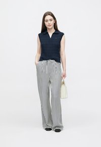 Mornarsko plavi pleteni top bez rukava s ovratnikom, u kombinaciji s crno-bijelim širokim hlačama s prugama. Uz to kremasta torba kao dodatak.