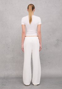 Witte cropped t-shirt en crèmekleurige wijde broek van zachte stof, met een elastische tailleband en een eenvoudig ontwerp.