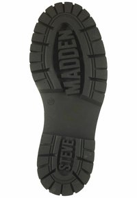 Suela de goma negra con un patrón de relieve grueso, que presenta el texto elevado "STEVE" y "MADDEN". Forma ovalada y plana con un diseño robusto. Talla 37.