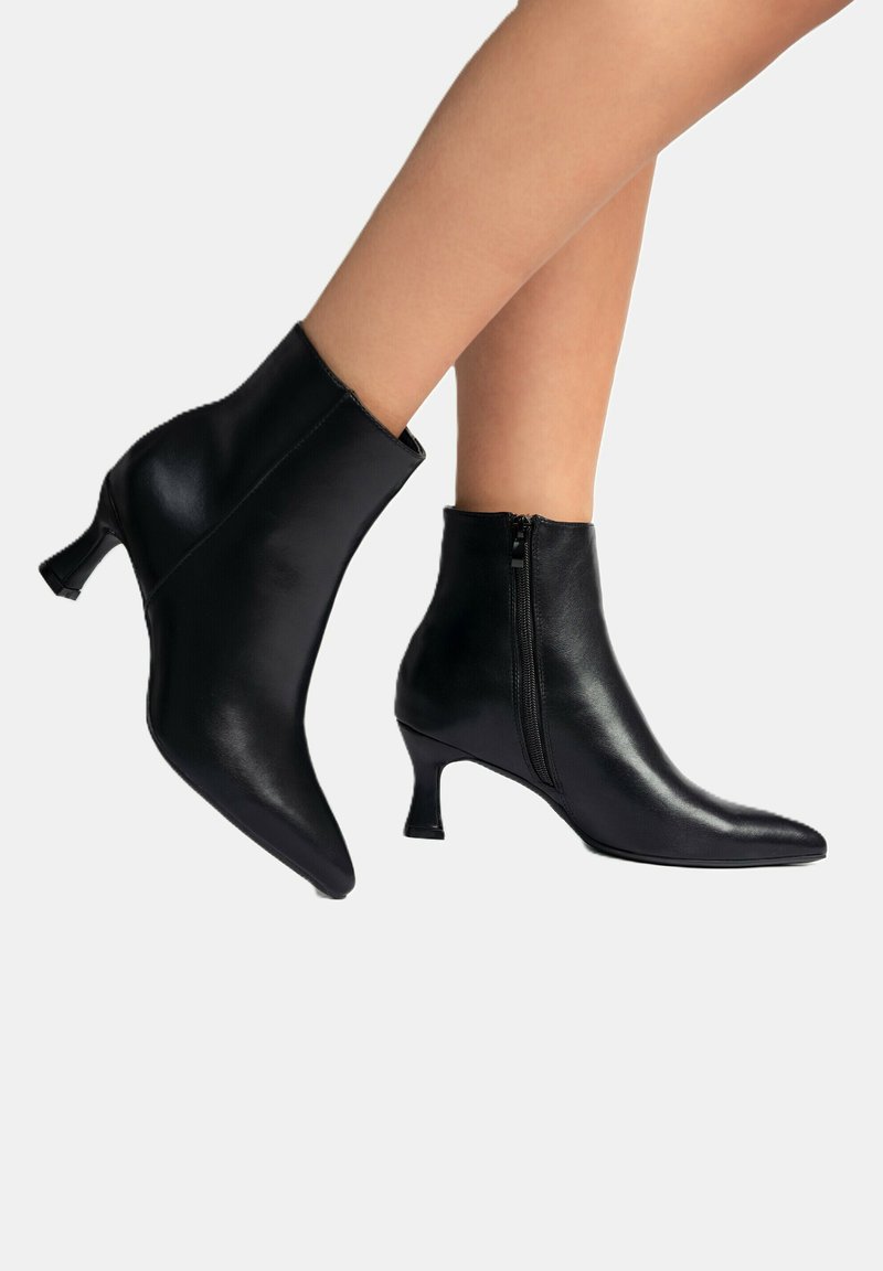 Schwarze Leder-Ankle Boots mit spitzen Zehen und kurzen, gestapelten Absätzen. Sie verfügen über einen seitlichen Reißverschluss und eine glatte, glänzende Oberfläche.