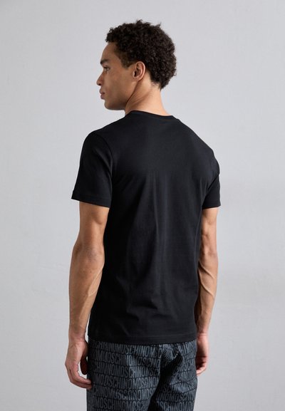 Svart t-skjorte i bomull med rund hals og korte ermer, sett bakfra. Brukes sammen med mønstrede grå joggebukser med logo-print.