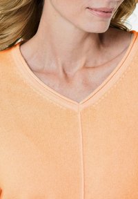 V-Ausschnitt Pullover aus weichem orangefarbenem Strick. Verfügt über ein dezentes Texturmuster und feine Nähte entlang des Halsausschnitts. Glattes, leichtes Material.
