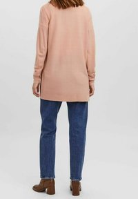 Ljusrosa, ribbad långärmad tröja med en avslappnad passform, kombinerad med blå raka jeans och bruna klackstövlar.