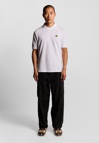 Vit texturerad polo med en subtil v-ringning och en liten broderad logotyp, kombinerad med svarta cargobyxor och mönstrade sneakers.