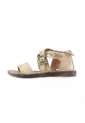 Sandalo piatto in camoscio beige con punta aperta, cinturino alla caviglia con fibbia metallica e borchie, e suola scura leggermente consumata.