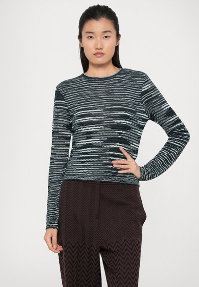 Pulover cu maneci lungi, texturat, în nuanțe de albastru și negru, cu dungi orizontale îndrăznețe. Împerecheat cu pantaloni largi, întunecați, cu un model.