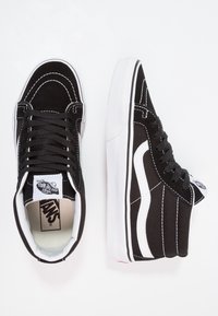 Czarno-białe trampki Vans w stylu high-top z białym przeszyciem i paskiem po bokach, pokazane z widoku z góry i z boku na białym tle.