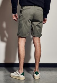 Khaki bavlněné šortky s ohrnutými manžetami, zadními kapsami a středním pasem, doplněné o bílé tenisky a zelené akcenty.