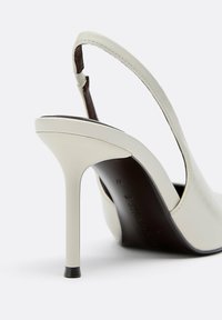 Chaussure blanche à talon haut slingback avec talon pointu, finition lisse et arrière ouvert, présentée sur un fond clair uni.