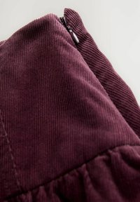 Țesătură de catifea bordeaux cu fâșii verticale, având un detaliu cu fermoar în partea de sus și accente stranse de-a lungul marginii de jos.