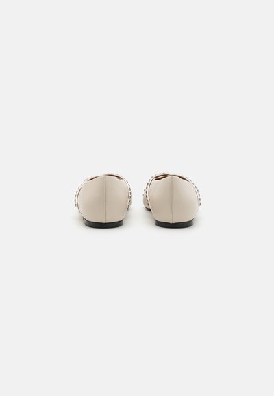 Ballerines en cuir beige avec un bout arrondi et une semelle noire, ornées de couture décorative le long du bord. Texture minimaliste et lisse.