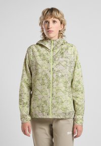 Veste légère à capuche de couleur vert p âle avec des taches noires. Dotée d'une fermeture éclair à l'avant et de poignets ajustés. Matériau lisse et résistant à l'eau.