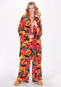 Wielokolorowy zestaw kimona i spodni szerokich nogawkach, z wyrazistymi okrągłymi wzorami w czerwonym, żółtym, zielonym i czarnym kolorze, zestawiony z pomarańczowymi sandałami na platformie.
