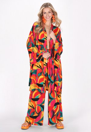 Multifarvet kimono og sæt med vide bukser, der har dristige cirkulære mønstre i rød, gul, grøn og sort, parret med orange platform sandaler.