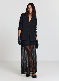 Blazer noir à revers cranté, associé à une jupe en dentelle noire transparente. Comprend des gants noirs et des escarpins noirs élégants. Détail en dentelle texturée.