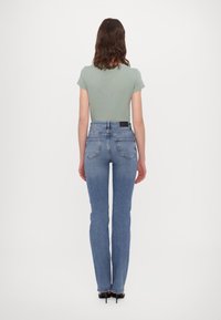 Camiseta ajustada verde claro, combinada con jeans de tiro alto azules. Los jeans tienen un corte recto clásico y bolsillos traseros con detalles de costura.