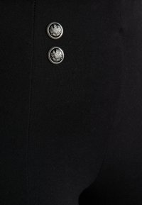 Leggings negros con dos botones decorativos plateados de diseños intrincados, textura suave y forma ajustada.