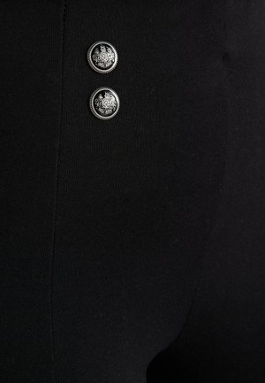 Legging noirs ornés de deux boutons en argent aux motifs complexes, texture lisse et coupe ajustée.