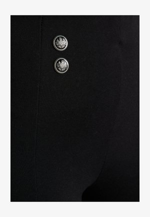 Legging noirs ornés de deux boutons en argent aux motifs complexes, texture lisse et coupe ajustée.