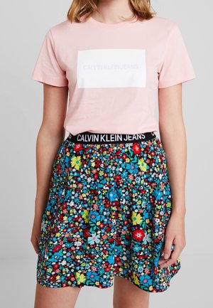 Lyserød bomulds-t-shirt med hvidt Calvin Klein Jeans-logo, kombineret med et sort elastisk taljebånd blomstret nederdel med flerfarvede blomster.