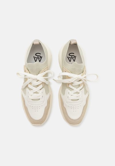 White and beige athletic shoes made of mesh and leather, featuring laces, perforations on the toe, and a cushioned sole.