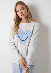 Lichtgrijze longsleeve shirt met een blauwe hartgrafiek en een glimlachend gezicht. Zachte stof, ontspannen pasvorm,Minimalistisch ontwerp.