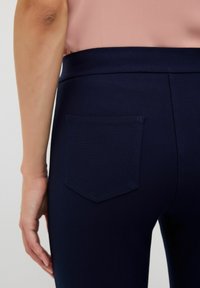 Mörkblå byxor med en slät yta, som har en enda bakficka med rektangulär design och en bred midjeband.