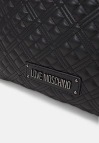 Czarna, pikowana skórzana powierzchnia z metalową tabliczką z nazwą marki "LOVE MOSCHINO", przymocowaną czterema nitami.