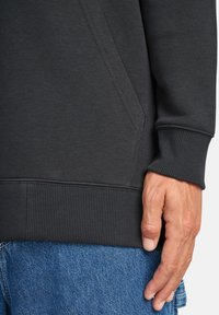 Donkergrijze sweatshirt met ribgebreide zoom en mouwen, voorzien van een zijzak en een zachte textuur, gecombineerd met blauwe spijkerbroeken.