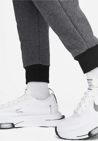 Bílé sportovní boty s texturovanými síťovanými panely a černými doplňky, kombinované se šedými tepláky s černým lemem u kotníku.