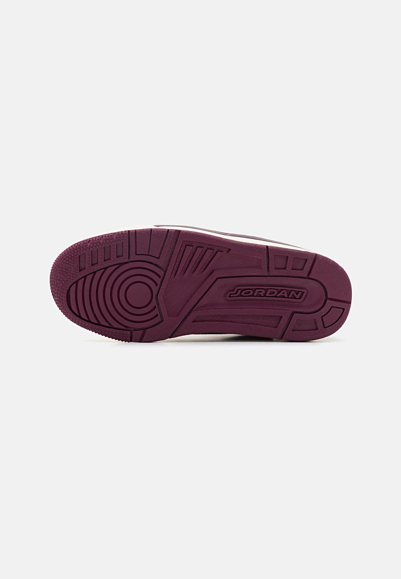 Suela de zapatilla de goma púrpura con patrones texturizados, agarre circular y nombre de la marca grabado. La sección superior blanca es parcialmente visible.
