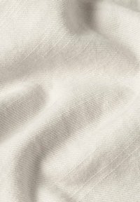 Nahaufnahme eines weichen, hellbeigen gewebten Stoffes mit feiner Textur und sanften Falten, die subtile Schatten und Lichtakzente erzeugen.