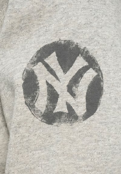 Zahtevna črna okrogla oznaka z prepletenima belima črkami "NY" natisnjena na svetlo sivi pleteni tkanini.