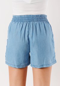 Pantaloni corti azzurri chiari con vita smock, dotati di tasche laterali e una vestibilità comoda. Il tessuto ha un aspetto morbido e testurizzato.