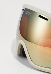 UV-védelemmel ellátott goggles fehér műanyag kerettel. A lencse zöld és narancs színátmenettel rendelkezik, a "POC" márkajelzéssel. Szivacsos párnázás tartozik hozzá.