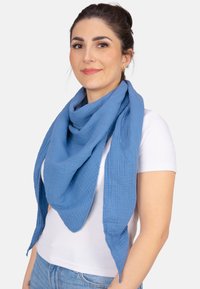 Écharpe en coton bleu clair avec un design texturé, drapée librement autour du cou. Présente des bords bruts et une forme triangulaire surdimensionnée.