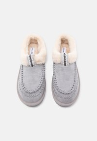 Grijze suède sloffen met een fluffy crèmekleurige kraag, voorzien van decoratieve stiksels en een gestructureerde rand. Zachte binnenvoering voor extra comfort.